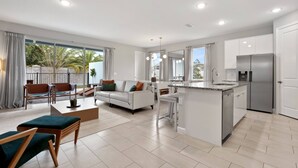 A modern open-plan living area with a kitchen, dining space, and a balcony with a view of palm trees. - 5BR townhouse with pool near Disney area (Kissimmee)