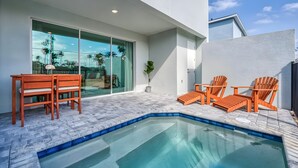A modern outdoor pool area with a glass-enclosed patio, wooden chairs, and a small table. - 5BR townhouse with pool near Disney area (Kissimmee)
