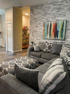A living room with a gray sectional sofa, patterned throw pillows, and a colorful abstract painting on the wall.