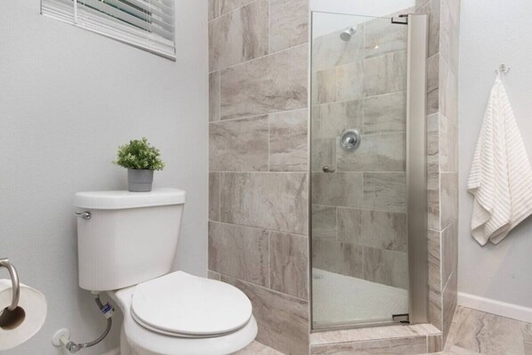 A bathroom with a toilet, a glass-enclosed shower, and a towel hanging on the wall.