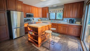 A kitchen with wooden cabinets, a stainless steel refrigerator, a microwave, a stove, and a large island with stools. - Mississippi River Home / HOT TUB / Sleeps 8 (Stoddard)