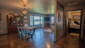 A spacious room with a wooden floor, a dining table with chairs, a chandelier, and a view of the outdoors. - Mississippi River Home / HOT TUB / Sleeps 8 (Stoddard)
