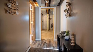 A hallway with wooden flooring, a wooden door leading to another room, and a console table with decorative items. - Mississippi River Home / HOT TUB / Sleeps 8 (Stoddard)