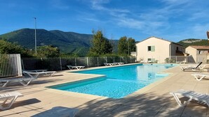 A swimming pool with lounge chairs, a mountain backdrop, and a building with a tiled roof.
