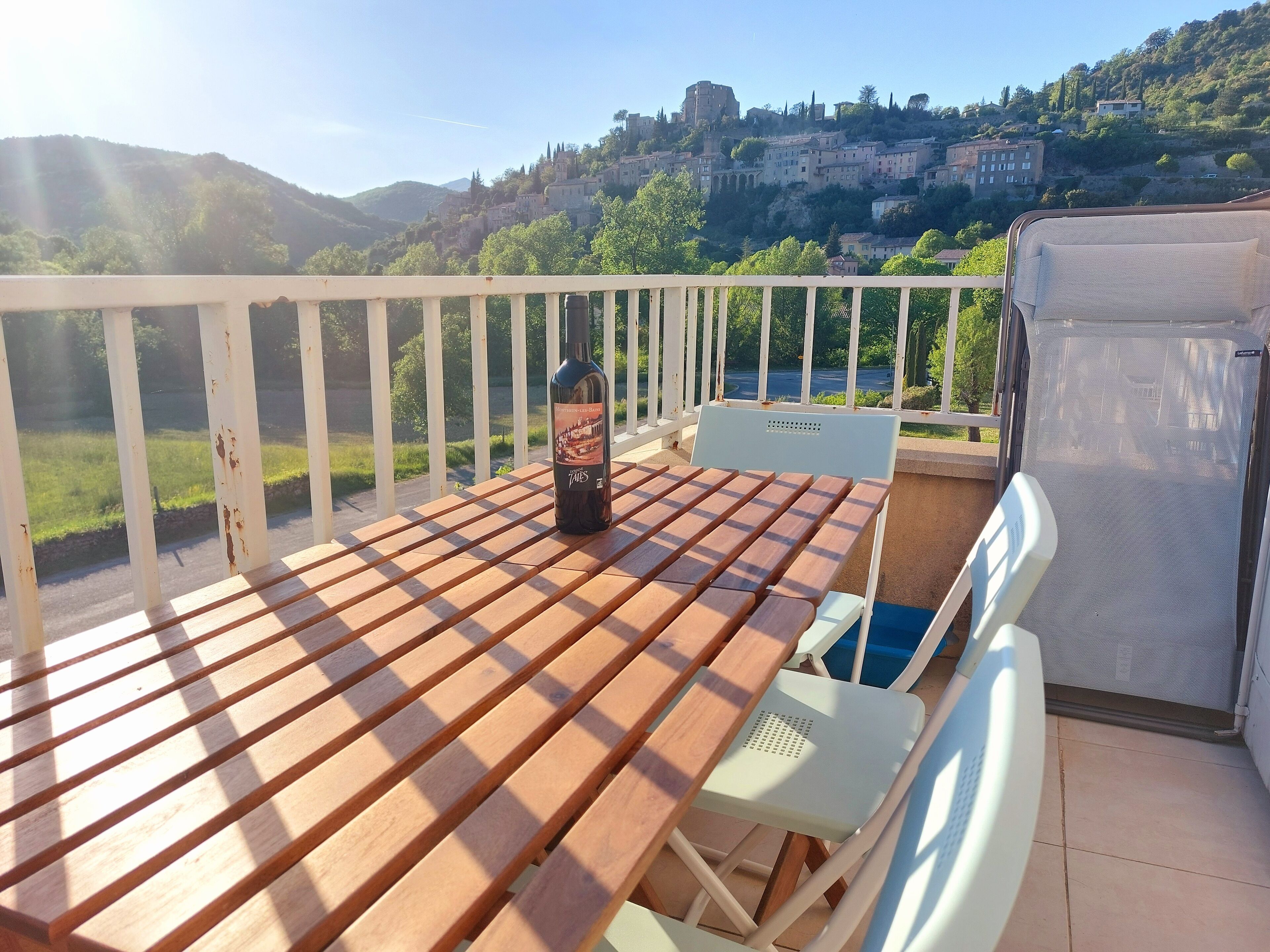 A wooden deck with a table and chairs, overlooking a scenic hillside with buildings.