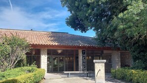 A building with a tiled roof and stone walls, featuring a large glass entrance and a stone pillar in the foreground.