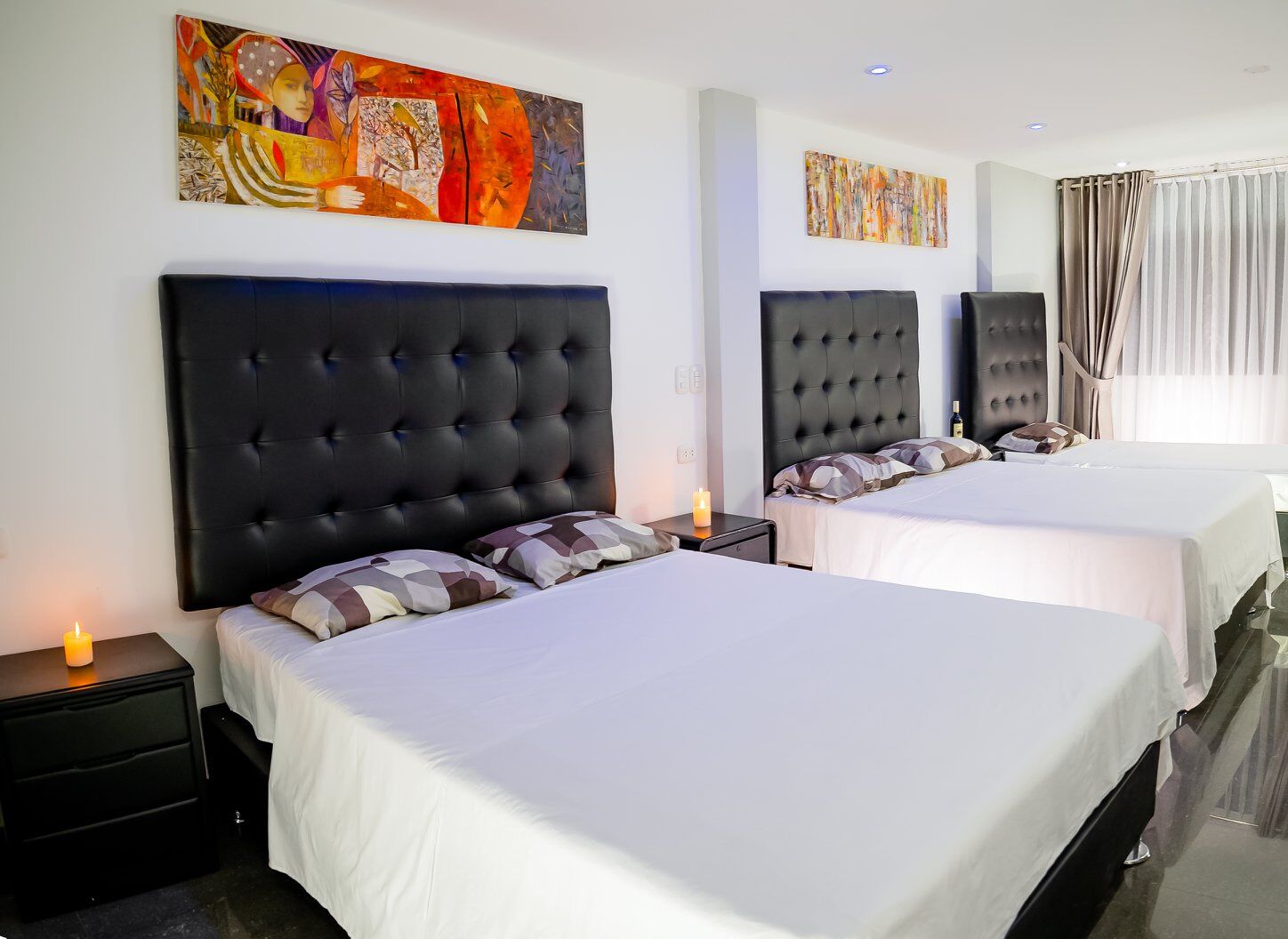 Une chambre d’hôtel avec deux lits, chacun doté d’une tête de lit noire, de draps blancs et d’une table de chevet sur laquelle se trouve une bougie. Deux tableaux abstraits ornent les murs.
