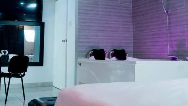 Une chambre d’hôtel moderne dotée d’un grand lit, d’un coin salon avec des fauteuils, d’une grande fenêtre et d’une salle de bain avec baignoire.