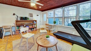 Ein gemütliches Zimmer mit Holzbalkendecke, Deckenventilator, Laufband, Bücherregal und großem Fenster.