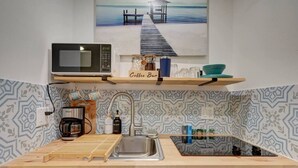 Eine Küche mit Mikrowelle, Kaffeemaschine und Spüle. Darüber befindet sich ein Regal mit einer Kaffeijar und einem Schild mit der Aufschrift 'Coffee Bar'.