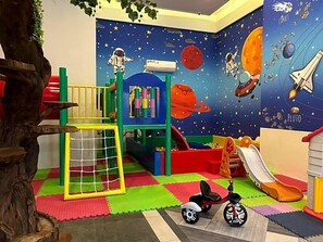 Ein Spielbereich mit Klettergerüst, Rutsche und Wandgemälde zum Thema Weltraum.
