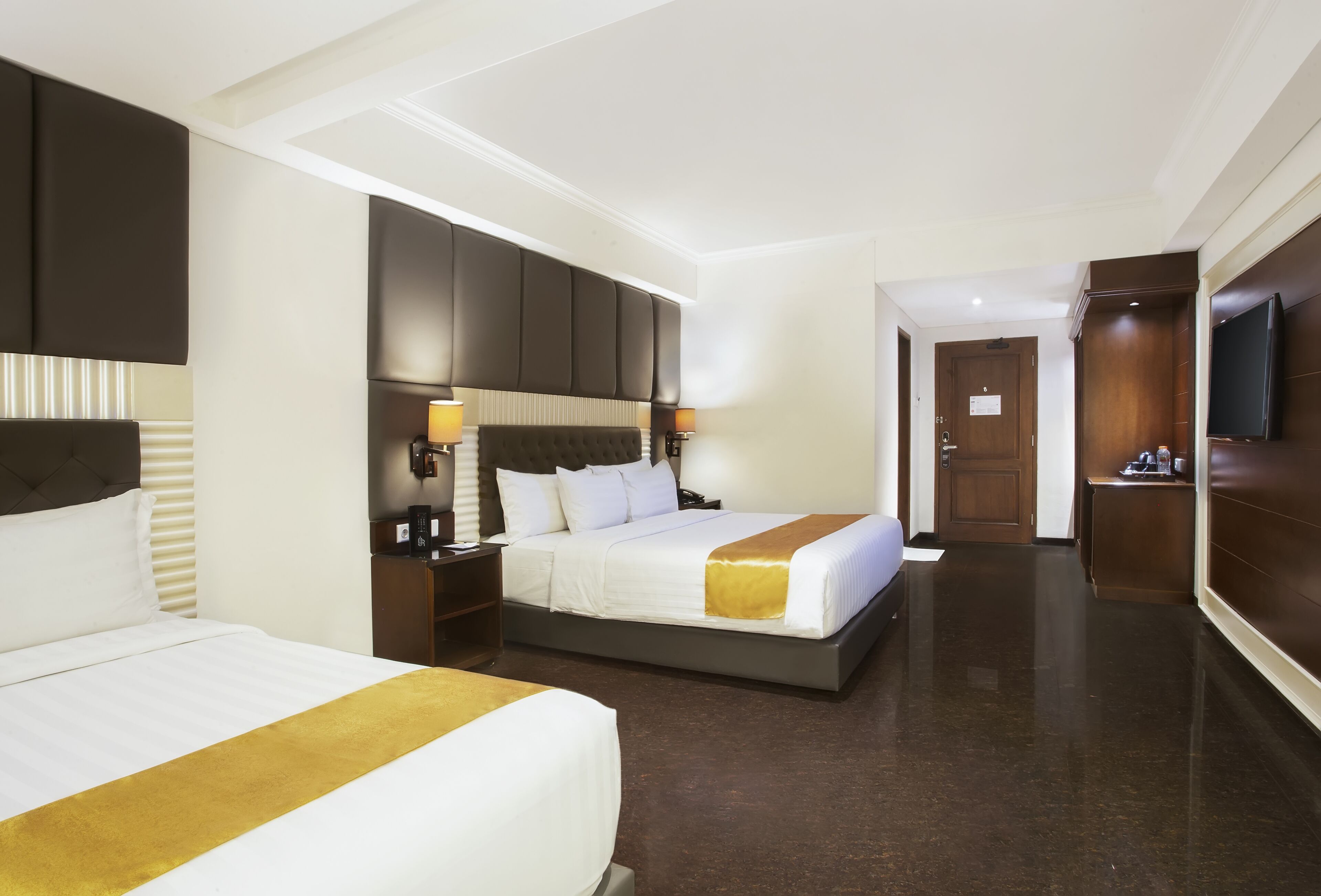 A hotel room with two beds, a large mirror, a TV, and a wooden wardrobe.