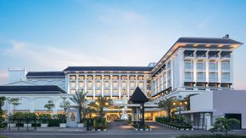 A large, multi-story hotel with a grand entrance, featuring a well-maintained garden and a prominent entrance gate.