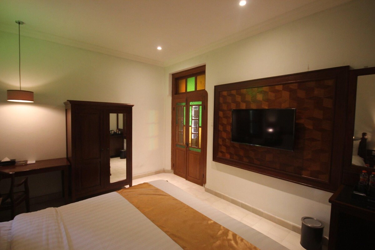 A bedroom with a bed, a desk, a wardrobe, a television mounted on the wall, and a door with glass panels.