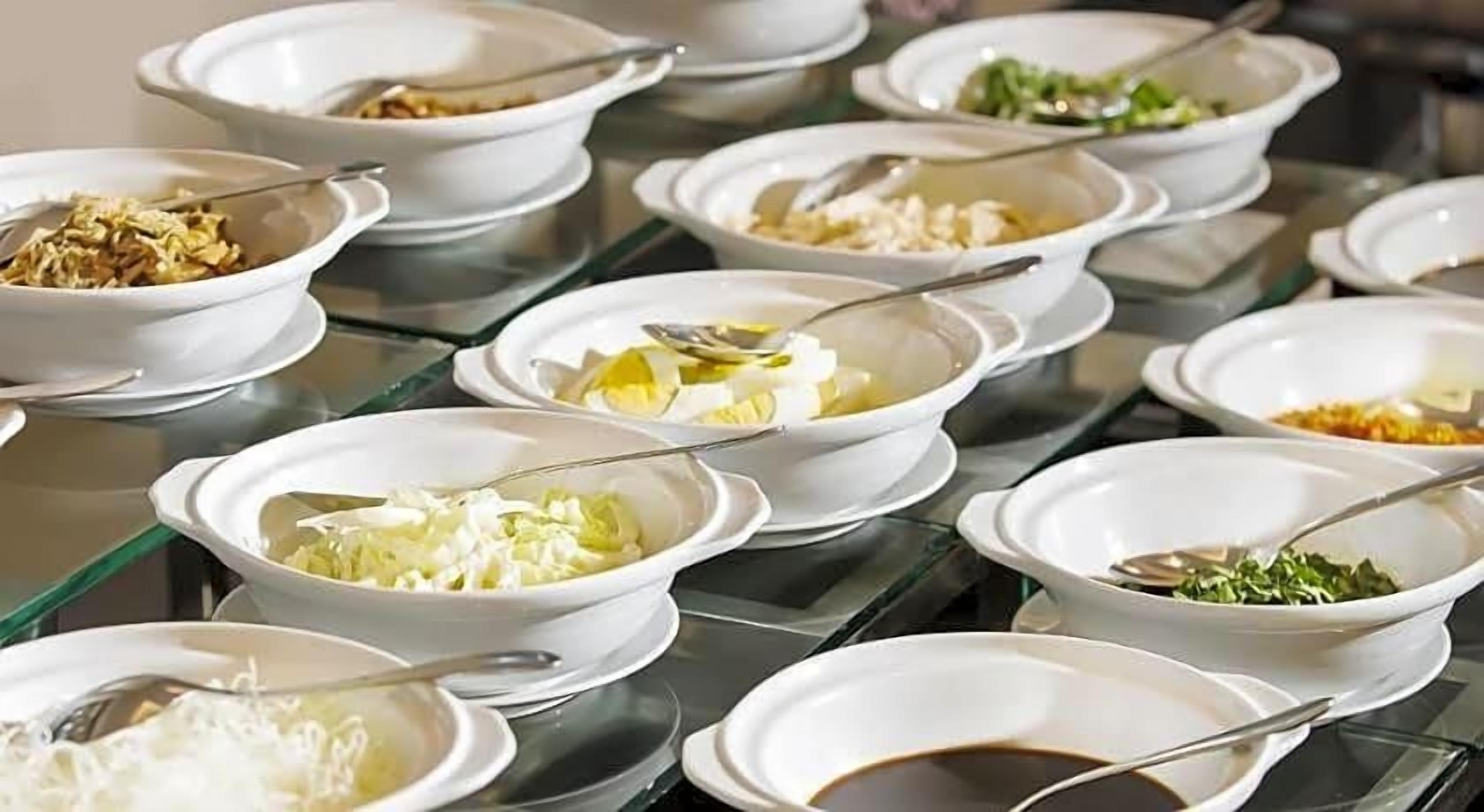 A buffet table with various dishes in white bowls, each with a spoon.