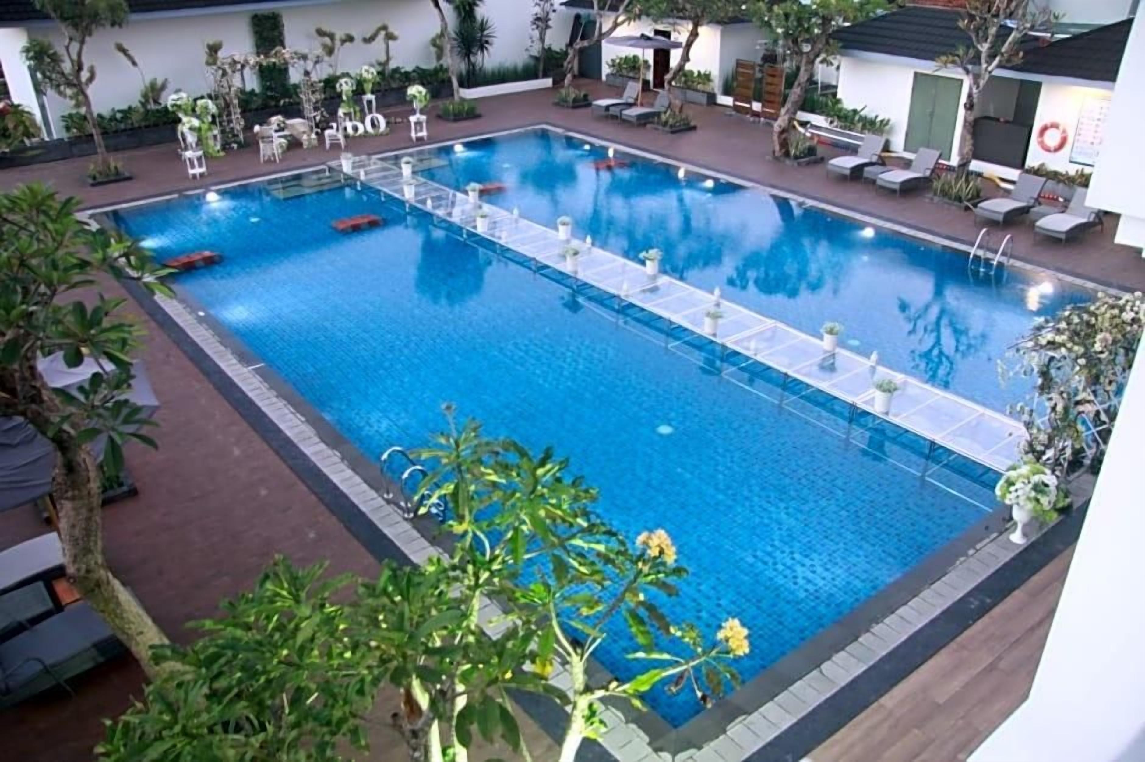 A rectangular pool with a clear blue water surface, surrounded by lounge chairs and potted plants.