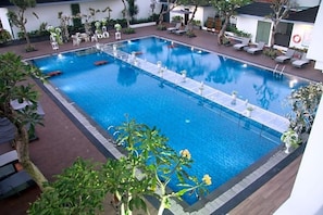 A rectangular pool with a clear blue water surface, surrounded by lounge chairs and potted plants. - Grand Rohan Jogja (Banguntapan)