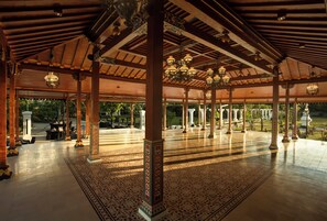 An indoor pavilion with a tiled floor and wooden beams, featuring ornate columns and hanging lamps.