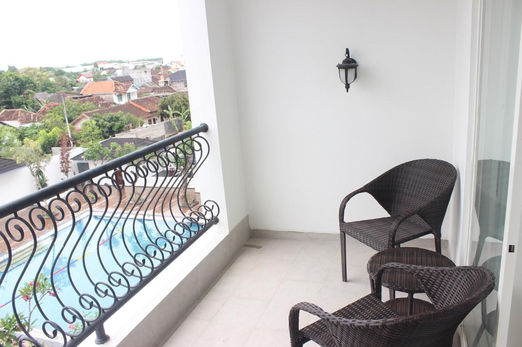 A balcony with a metal railing, a pool, and two wicker chairs.