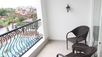 A balcony with a metal railing, a pool, and two wicker chairs.
