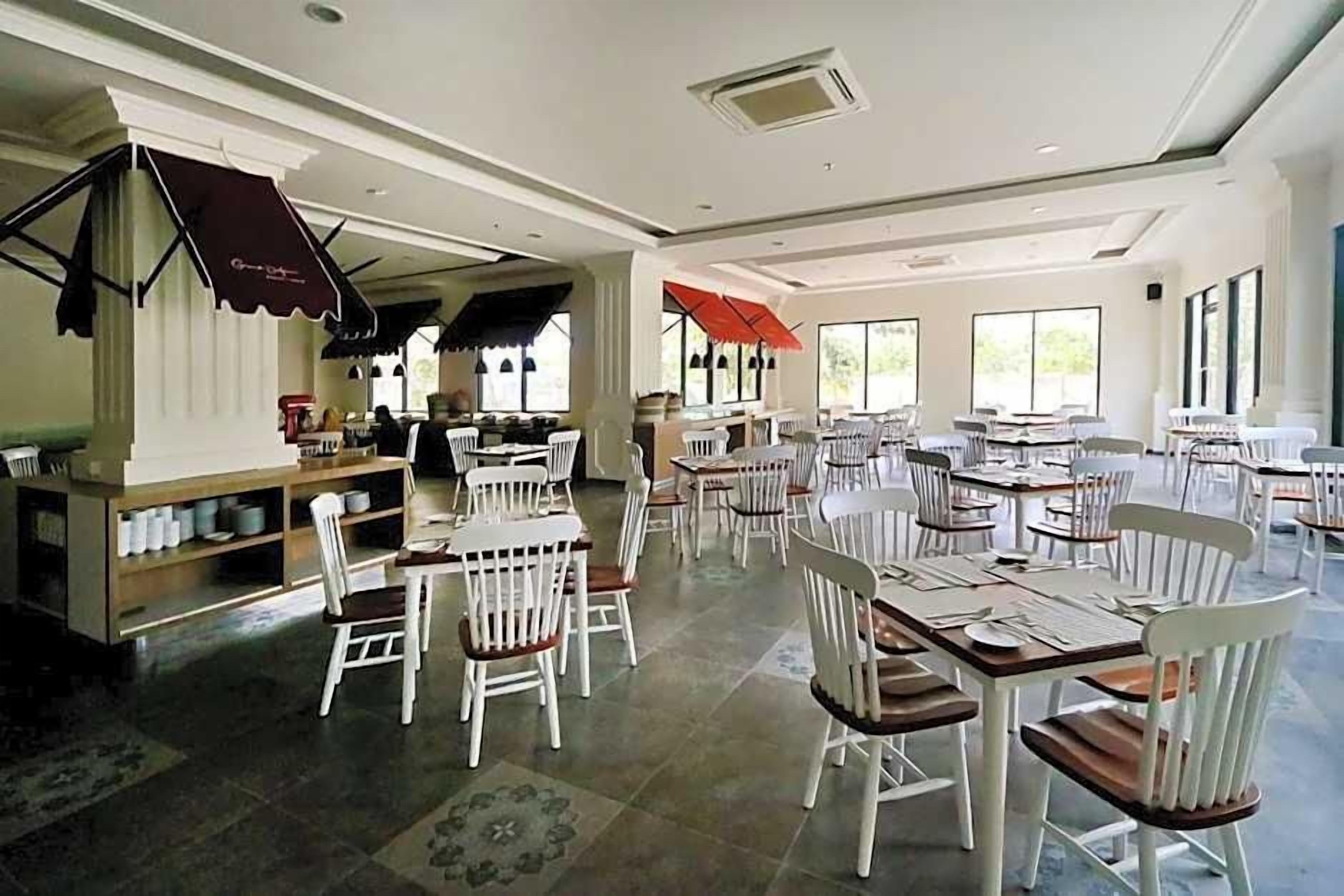 Um restaurante espaçoso com várias mesas e cadeiras, grandes janelas e decoração moderna.