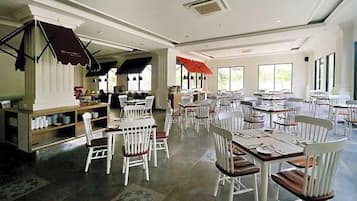 Um restaurante espaçoso com várias mesas e cadeiras, grandes janelas e decoração moderna.