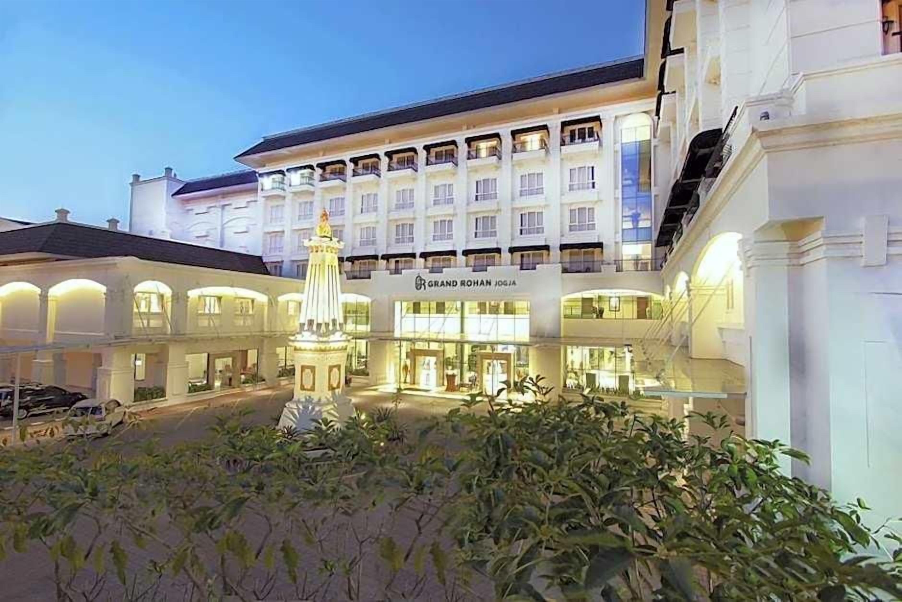 A hotel with a central courtyard, a prominent fountain, and a sign reading "Grand Rohan Jogja."