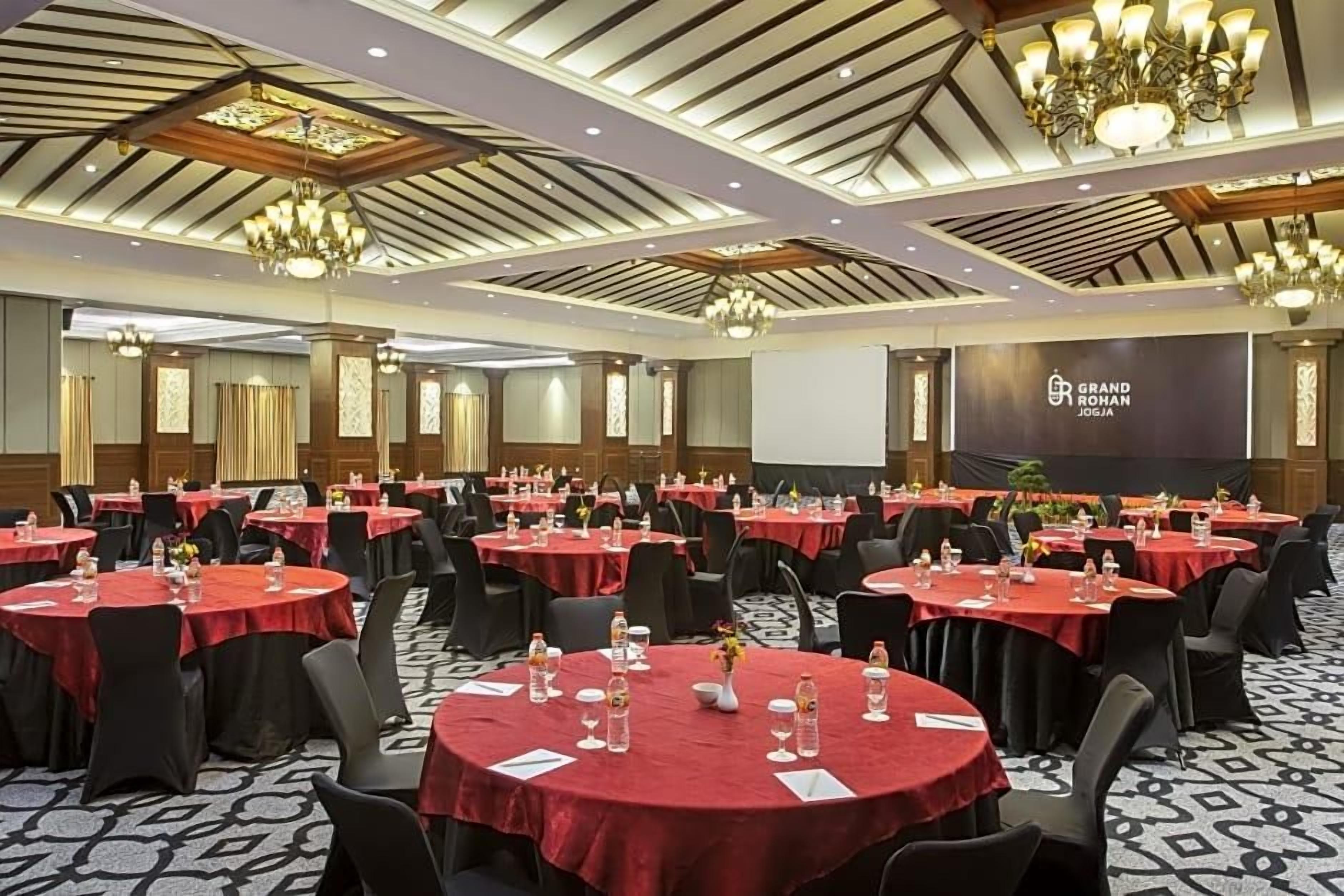 Un salón de conferencias con mesas redondas, sillas negras y manteles rojos.