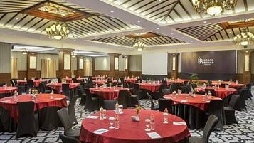 Un salón de conferencias con mesas redondas, sillas negras y manteles rojos.