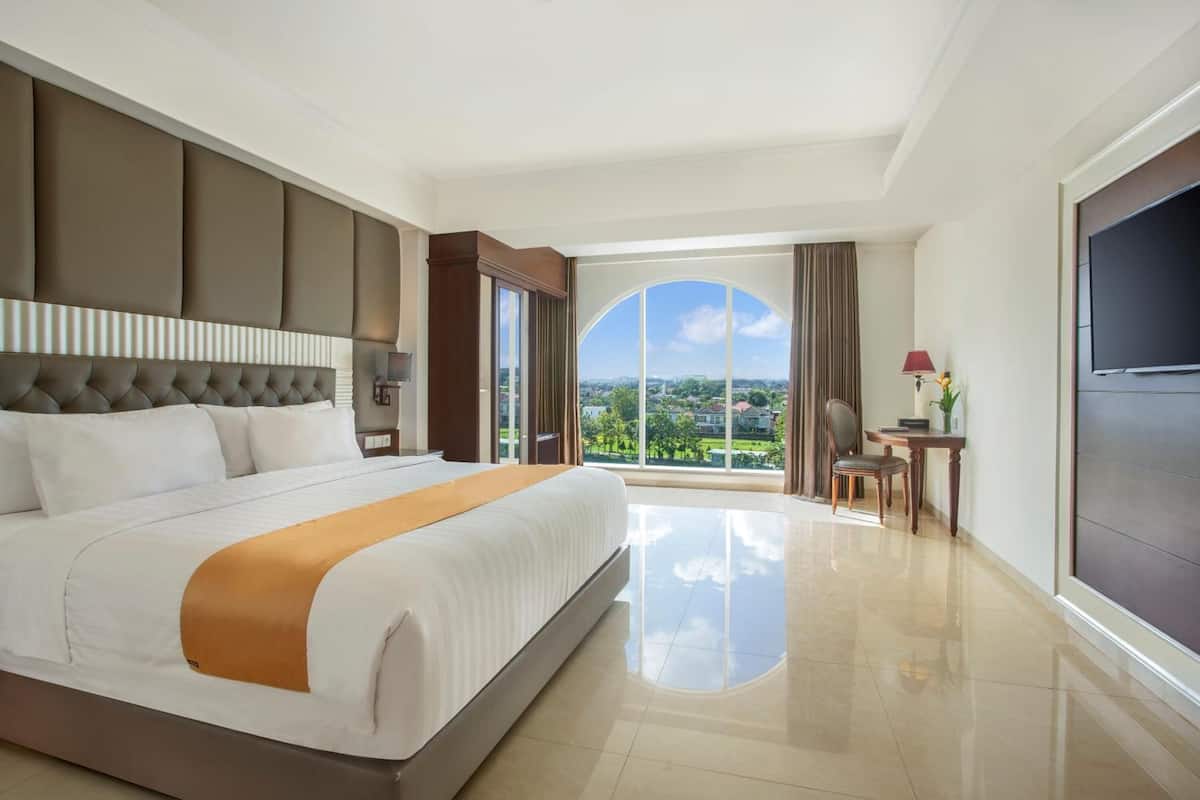 Quarto de hotel espaçoso com uma cama grande, vista para a cidade, escrivaninha e televisão.
