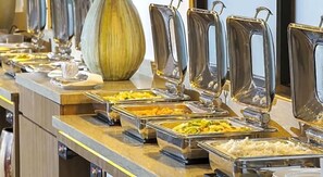 A buffet with various food items in metal containers, a large vase, and a modern counter design. - Grand Rohan Jogja (Banguntapan)