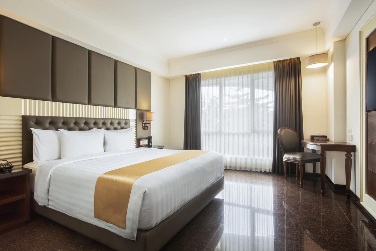 A hotel room with a large bed, a desk, a chair, and a window with curtains.