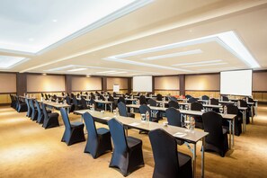 A conference room with rows of tables and chairs, equipped with water bottles and glasses, and a projector screen at the front. - Grand Rohan Jogja (Banguntapan)