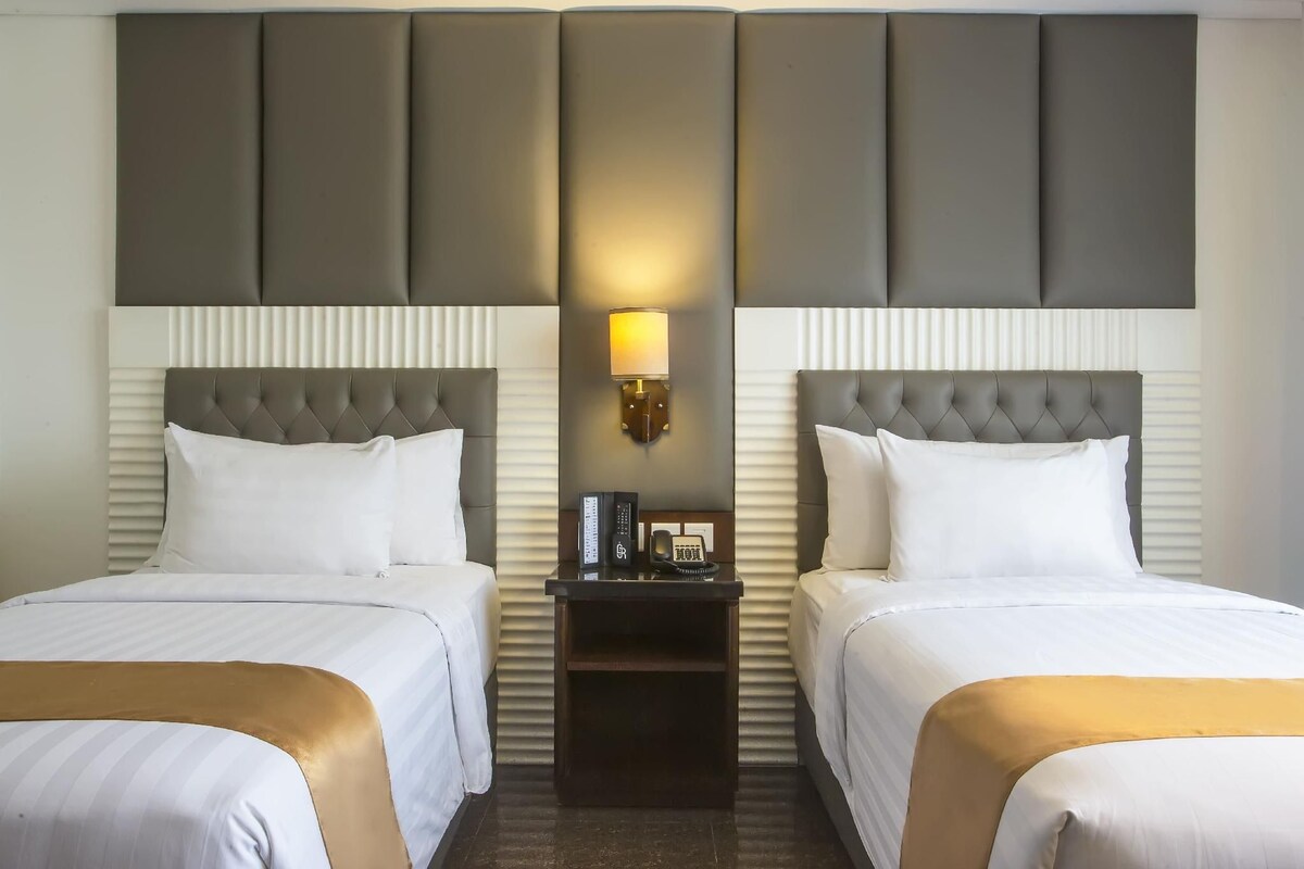 Ein Hotelzimmer mit zwei Betten, einem Nachttisch mit Lampe und einem an der Wand befestigten Telefon.