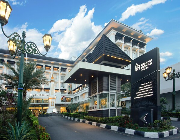 A hotel with a modern facade, multiple balconies, and a sign indicating amenities like a restaurant and a swimming pool.