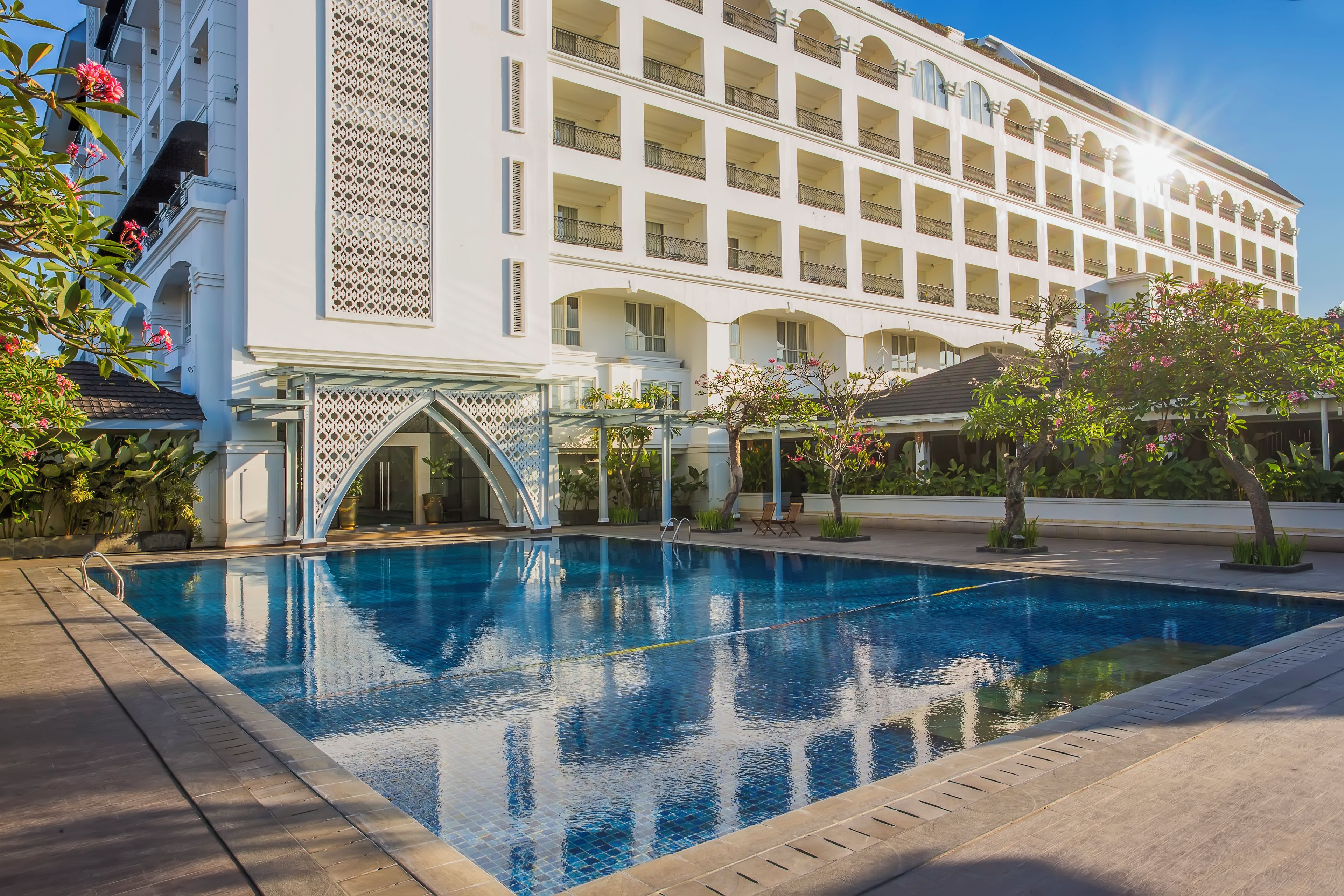 A large hotel with a swimming pool, multiple balconies, and a covered entrance.