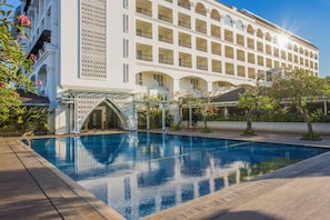 Een groot hotel met een zwembad, meerdere balkons en een overdekte ingang.