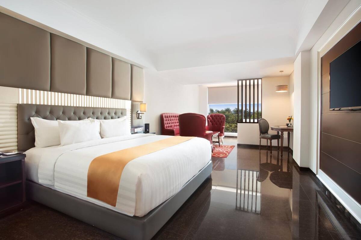 Quarto de hotel moderno com uma cama grande, televisão, varanda com assentos e vista para o exterior.
