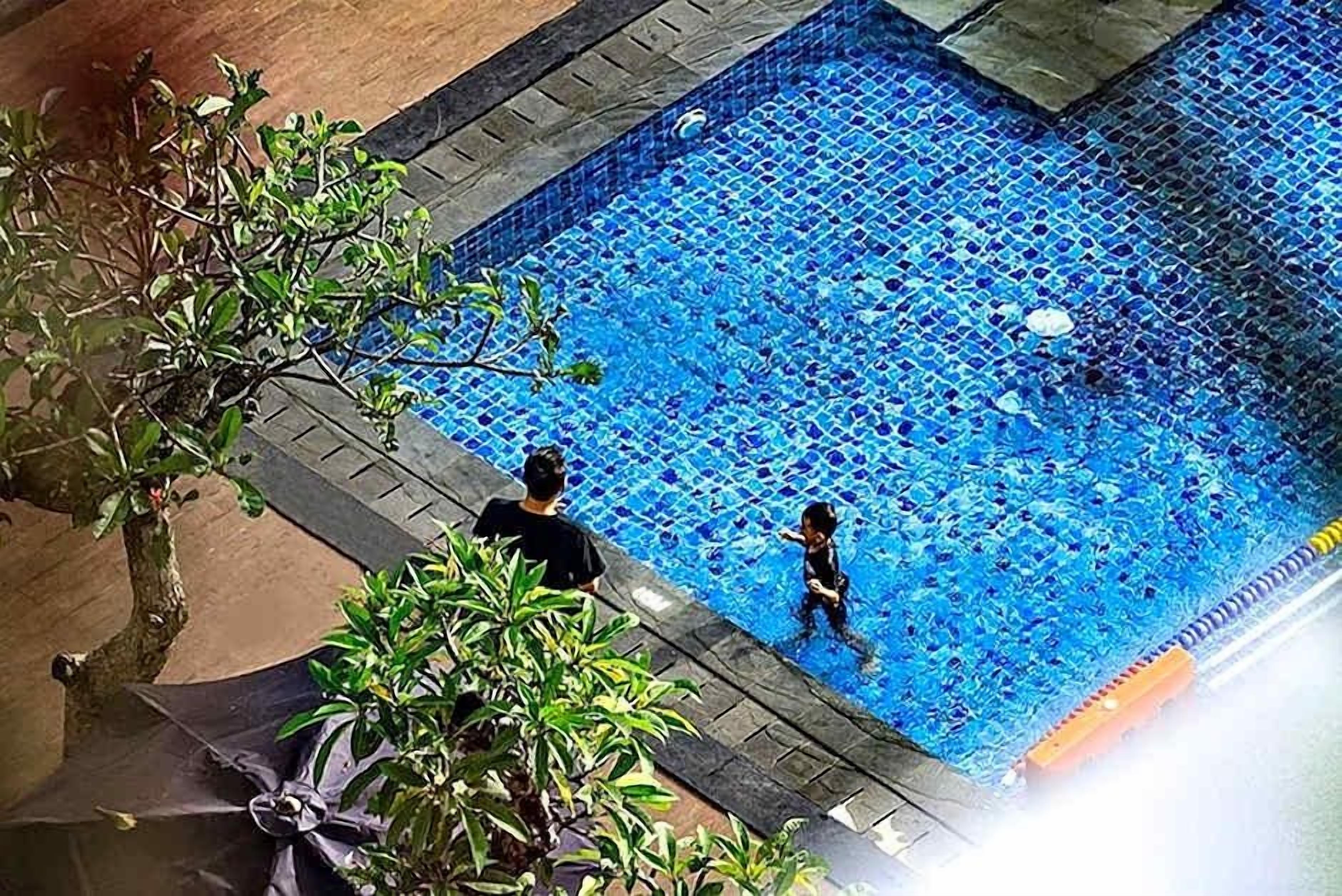 Une piscine dont le fond est recouvert de carrelage, avec une personne et un enfant dans l ’eau.
