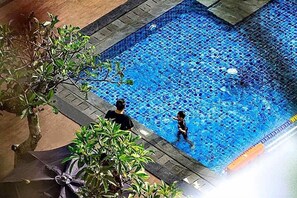 A swimming pool with tiled flooring and a person and child in the water.