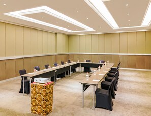 Una sala de conferències amb una taula llarga, cadires, ampolles d'aigua i una caixa amb dibuixos.