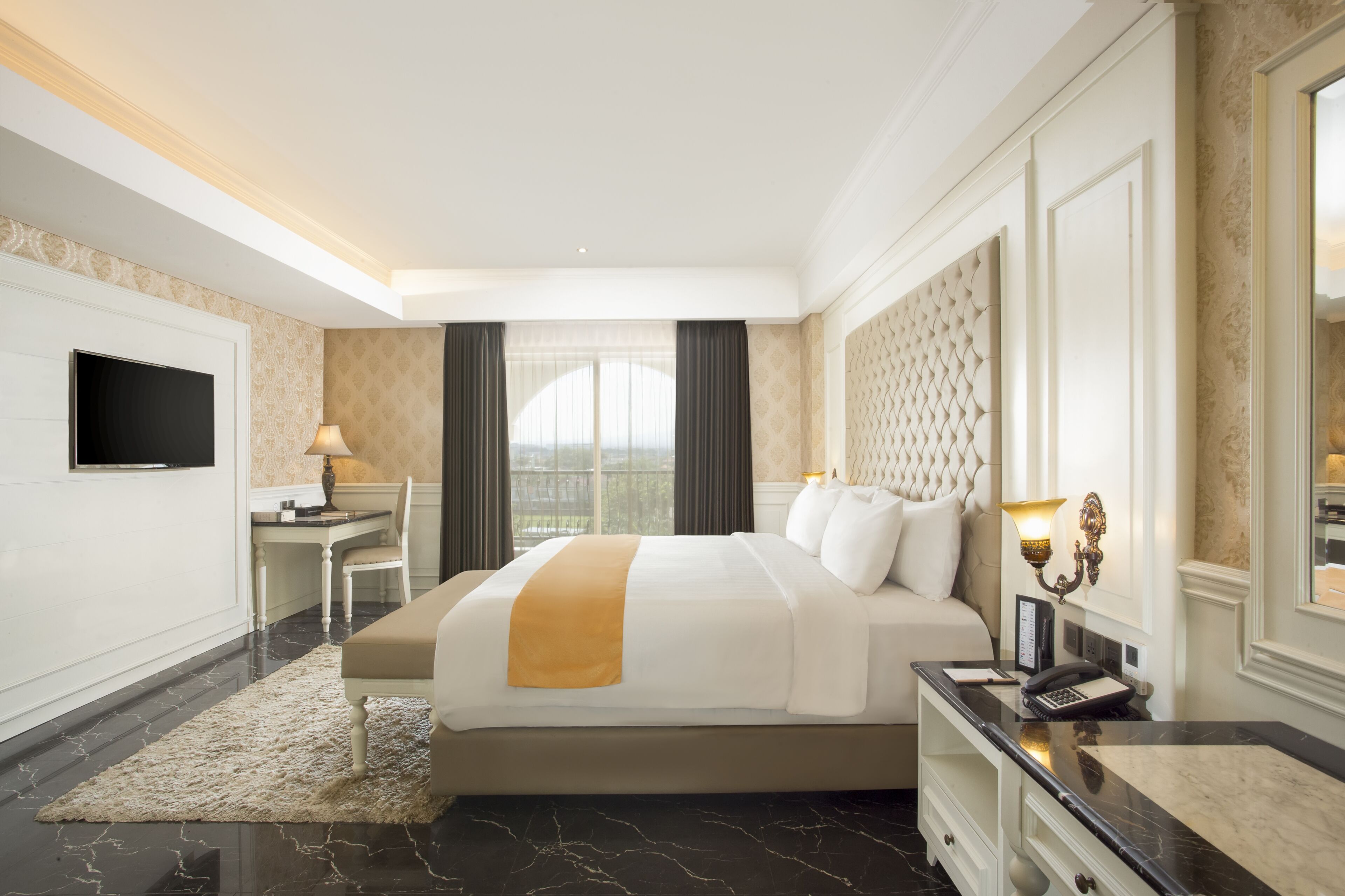 A hotel room with a large bed, a desk, a television, and a view of the city.