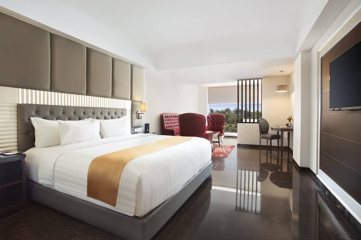 Quarto de hotel moderno com uma cama grande, uma escrivaninha, uma cadeira e uma televisão.