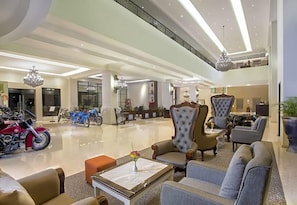 Un hall d’entrée spacieux avec de hauts plafonds, des lustres modernes et un coin salon agrémenté de fauteuils et de canapés confortables.