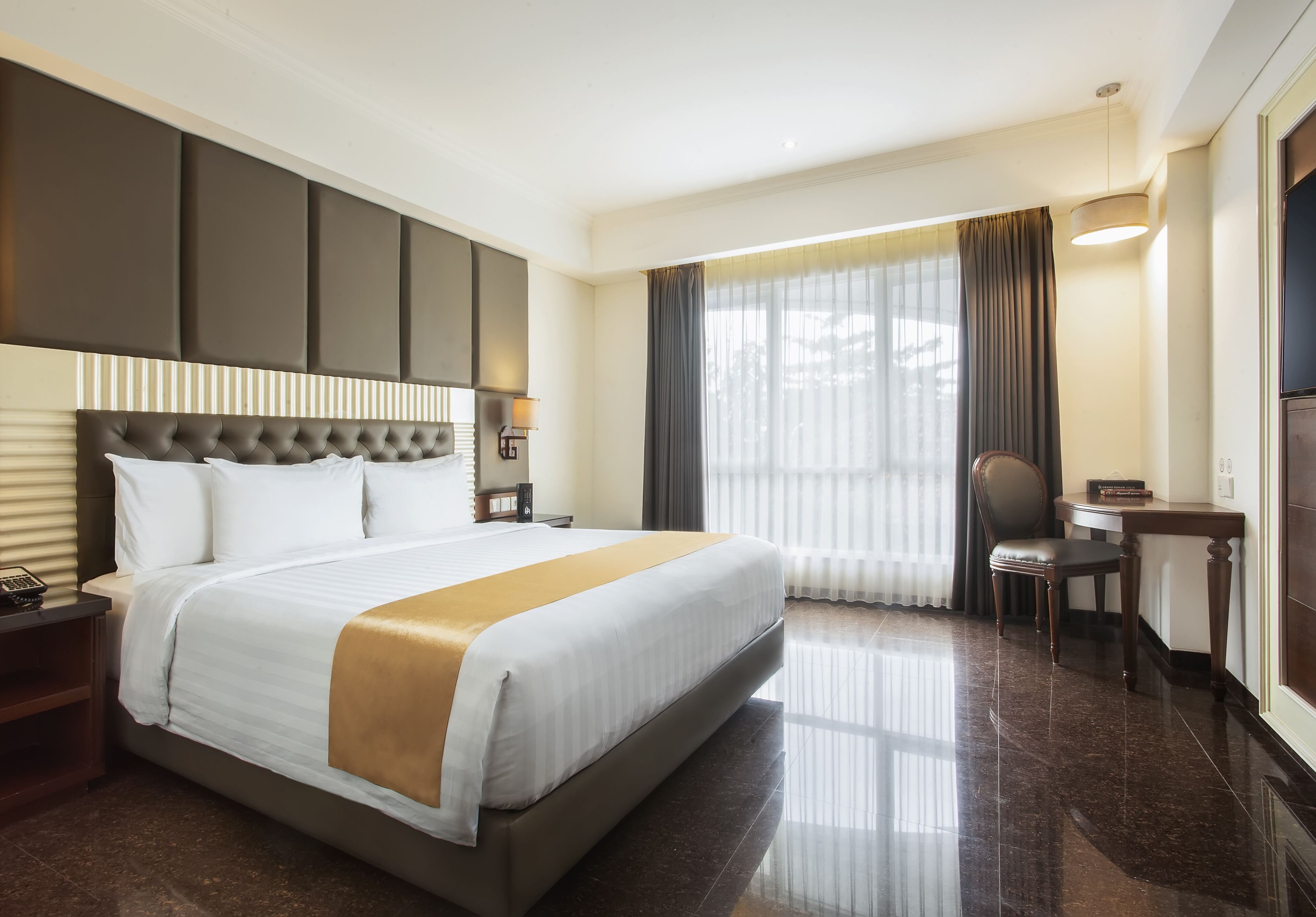 A hotel room with a large bed, a desk, a chair, and a window with curtains.