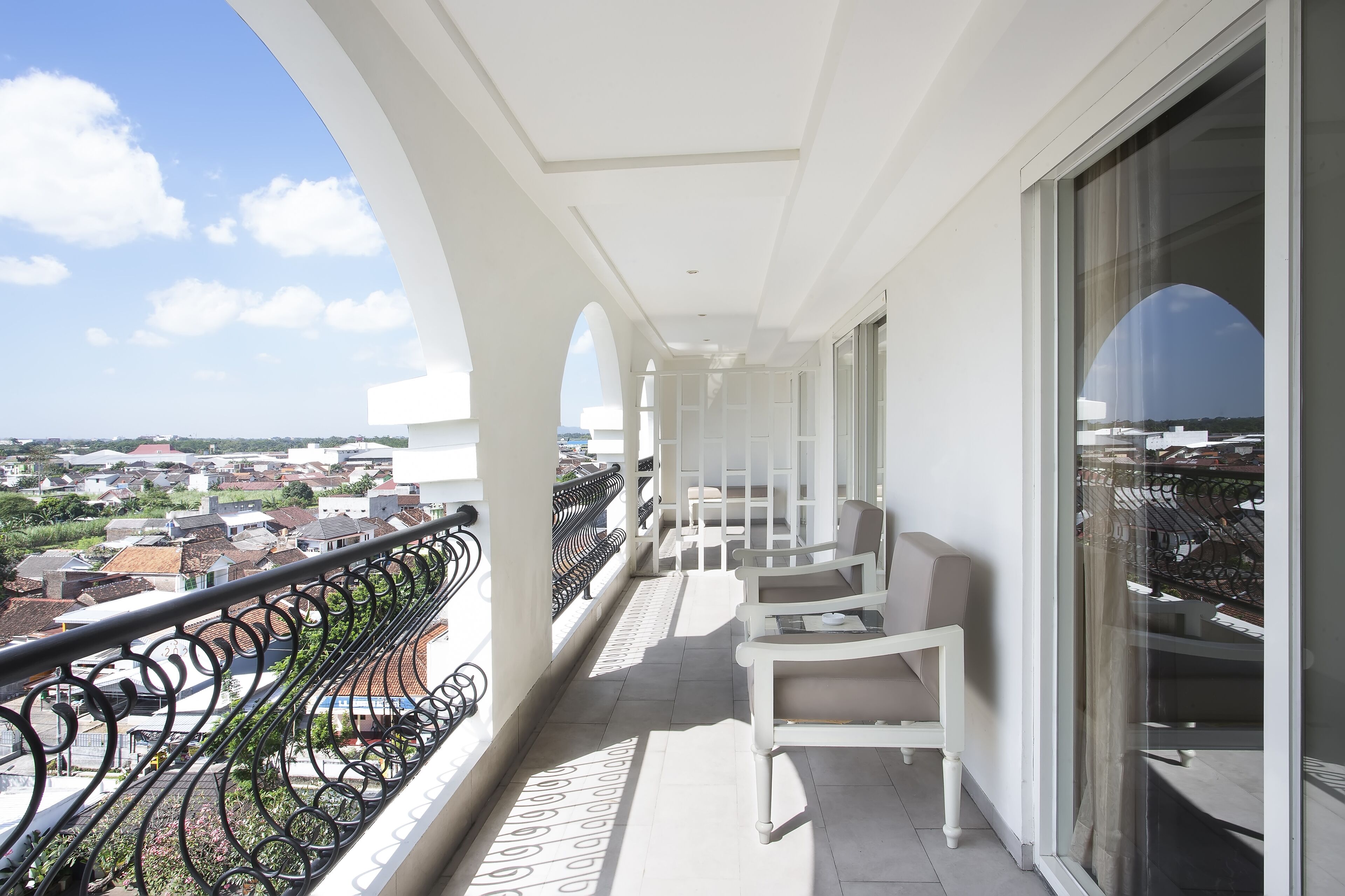 A balcony with white chairs and a black wrought iron railing, overlooking a residential area.
