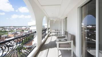 A balcony with white chairs and a black wrought iron railing, overlooking a residential area.