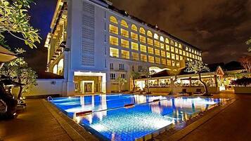 A hotel with a swimming pool, a large building with multiple windows, and a well-lit facade.