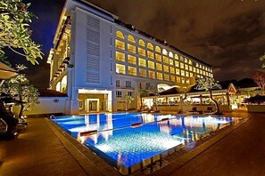 Un hotel con piscina, un edificio grande con múltiples ventanas y una fachada bien iluminada.