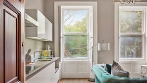 A compact kitchen with a window, a teal sofa, and a dining area.